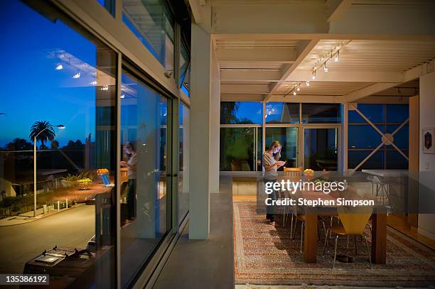 sunrise/sunset, modernist home, woman at table - modern house dusk stock-fotos und bilder