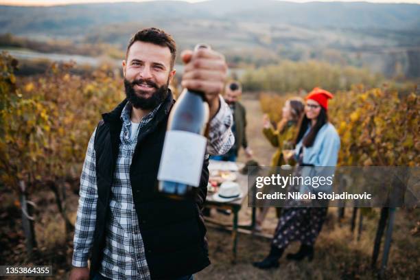 der junge besitzer des weinguts hält eine flasche wein in der hand - weinbar stock-fotos und bilder