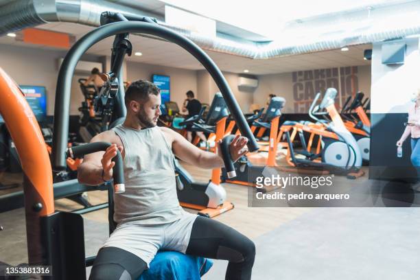 young man training his arms with a machine inside a gym - male chest stock pictures, royalty-free photos & images