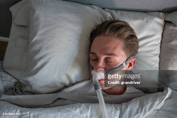 close up of a young man with sleep apnea wearing a cpap mask in bed sleeping on his side - sleep apnea stock pictures, royalty-free photos & images