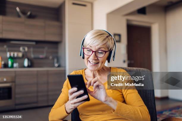 portrait of a mature woman with headphones enjoying surfing the net - podcast headphones stock pictures, royalty-free photos & images