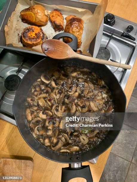 preparing homemade rustic mushroom soup, chopped organic mushrooms in farmhouse kitchen, chopping board and large pan on stove, button and chestnut and portobello mushrooms and porcini cooking on hob in kitchen in uk in april 2021 - white mushroom stockfoto's en -beelden