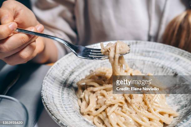 woman eats spaghetti in cheese sauce with black pepper at restaurant . traditional  roman pasta cacio e peppe in italy, italian cuisine recipes - macaroni and cheese stockfoto's en -beelden
