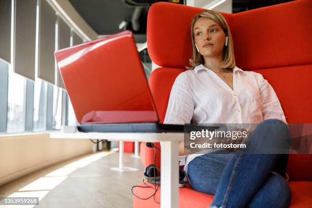 businesswoman resting in a cozy red armchair, listening to music and contemplating - red office chair stock pictures, royalty-free photos & images