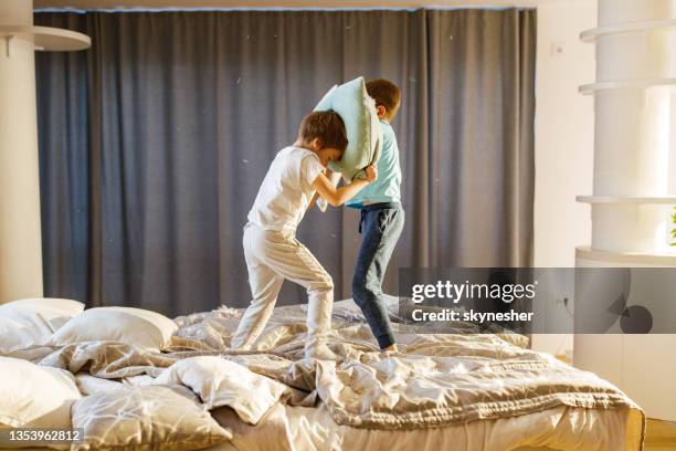 carefree boys having fun while fighting with pillows on a bed. - pillow fight stock pictures, royalty-free photos & images