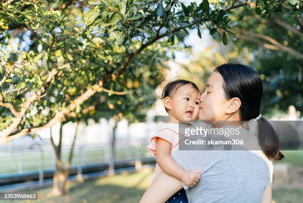 happiness togetherness positive emotion asian mother kissing her daughter and playing each other  front yard - asian mom kid kiss bildbanksfoton och bilder