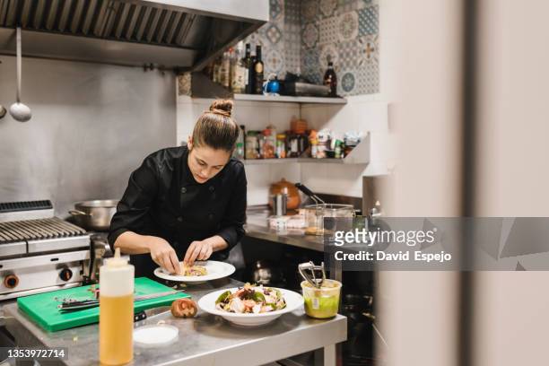 professional female chef garnishing and finishing a dish while working in a restaurant kitchen. - köchin stock-fotos und bilder