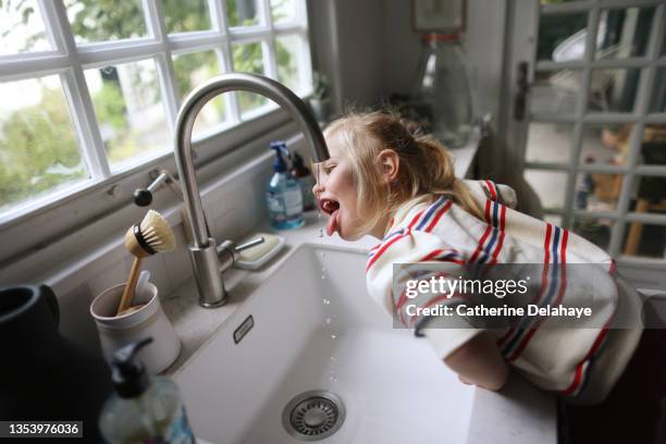 a little girl drinking water from the tap in the kitchen - wasser trinken zu hause stock-fotos und bilder