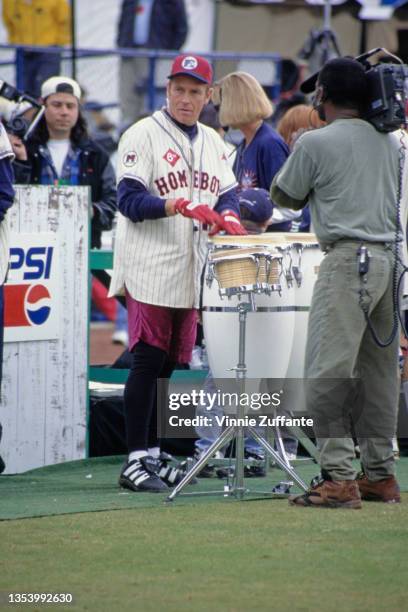 American actor Corbin Bernsen, wearing a 'Homeboys' kit, filmed playing a conga drum during MTV's 6th Annual Rock n' Jock baseball game, held at...