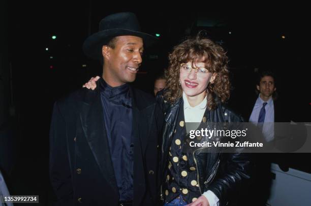 American actress and comedian Sandra Bernhard, wearing a black leather jacket and black waistcoat with gold polka dots, poses with a man outside...