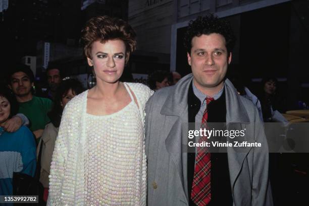 American actress and comedian Sandra Bernhard, wearing a white minidress, and American fashion designer Isaac Mizrahi, wearing a grey raincoat over a...