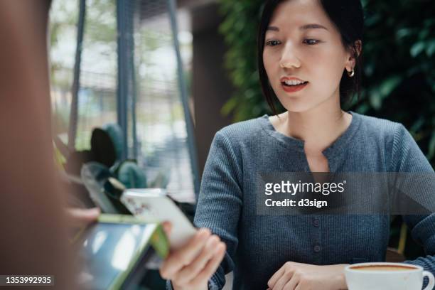 close up of young asian woman making mobile payment with her smartphone in a restaurant, scan and pay a bill on a card machine making a quick and easy contactless payment. nfc technology, tap and go concept - nfc payment stock pictures, royalty-free photos & images