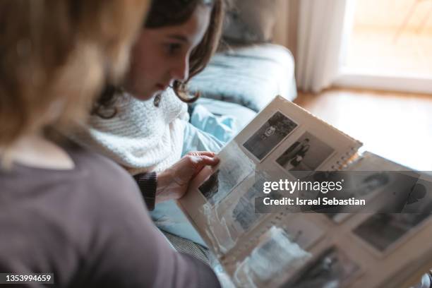 grandmother sharing memories with her granddaughter while showing old family photo album to her. - looking at old photo stock pictures, royalty-free photos & images