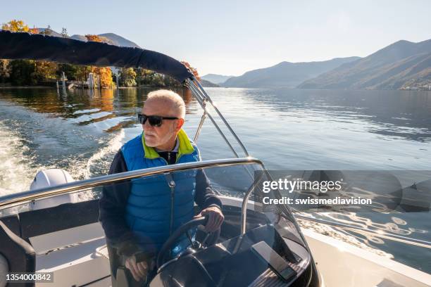 reifer mann steuert im herbst boot auf dem see - motorboot stock-fotos und bilder