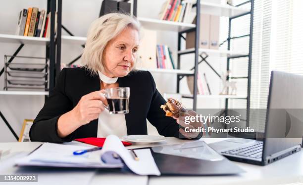 femme âgée mangeant un beignet pendant sa pause - desire stock photos et images de collection