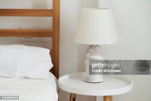 close-up of white lamp on bedside table inside a white walled room. - bedside table lamp stock pictures, royalty-free photos & images