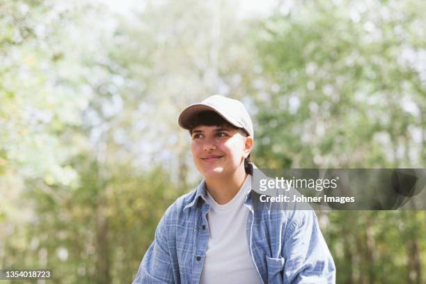 young woman wearing baseball cap smiling in forest - androgynous stock-fotos und bilder