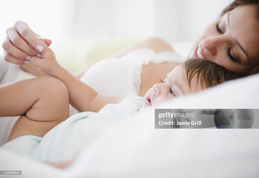 Mother holding baby's hand in bed