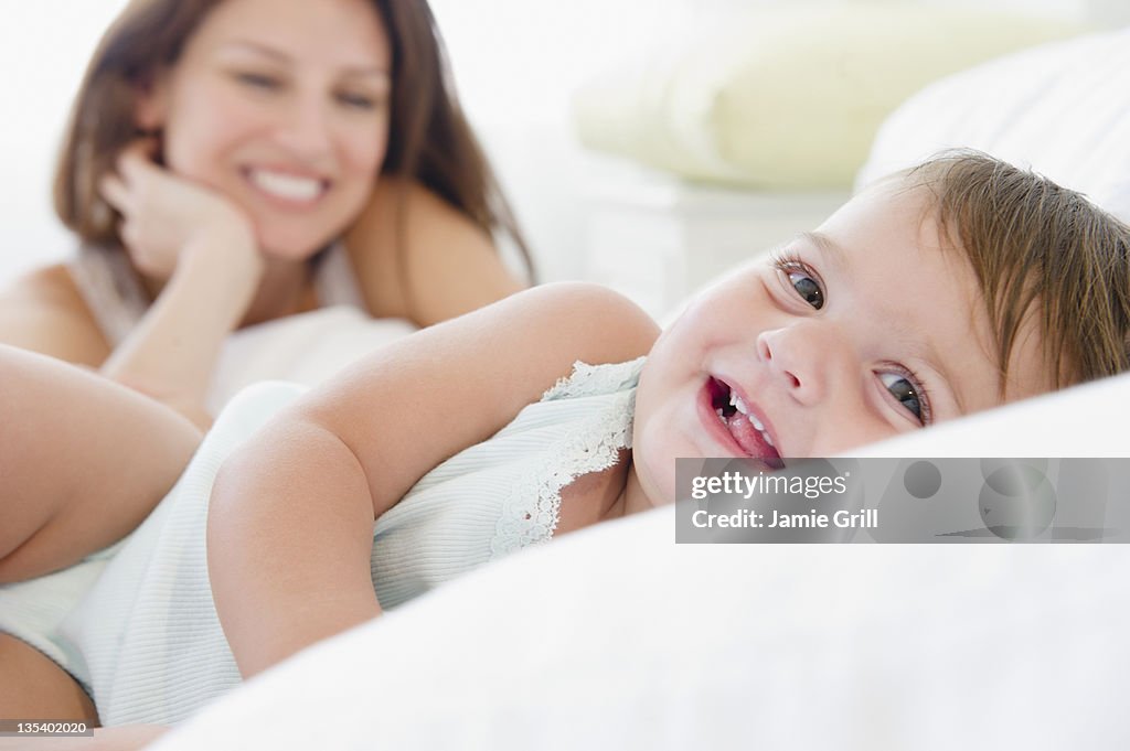 Baby smiling, mother watching in background