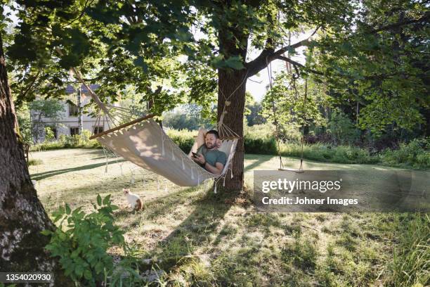 man lying in hammock in garden - hammock foto e immagini stock