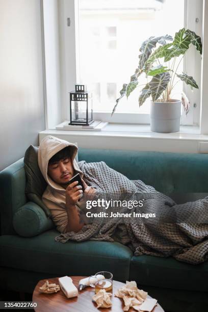 ill man on sofa using cell phone - sick person on phone stock pictures, royalty-free photos & images