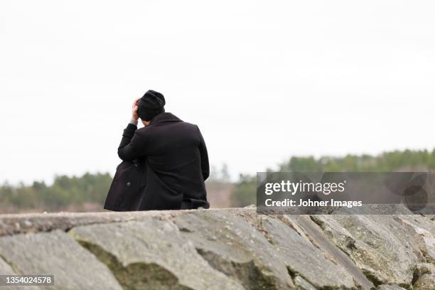 man sitting on stone groyne - lonely man stockfoto's en -beelden