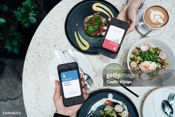 top view of friends splitting bill, sending / receiving the payment of the meal through digital wallet device on smartphone while dining together in a restaurant. smart banking with technology - paying for dinner imagens e fotografias de stock