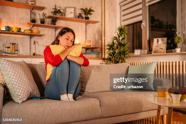 sad woman sitting on sofa embracing pillow - woman curled up stock pictures, royalty-free photos & images