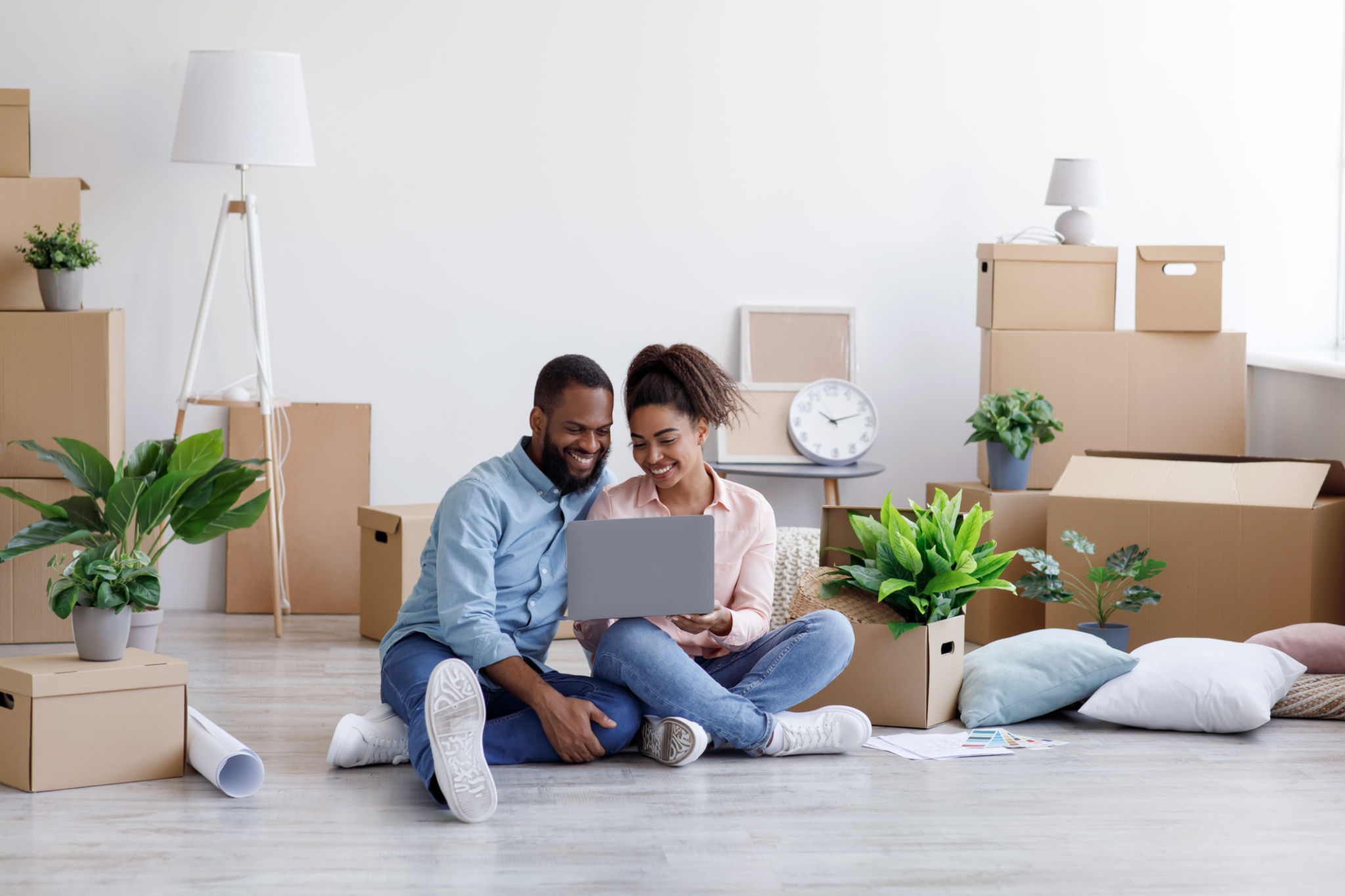 Glad young african american family resting, sitting on floor among cardboard boxes with things Glad young african american family resting, sitting on floor among cardboard boxes with things