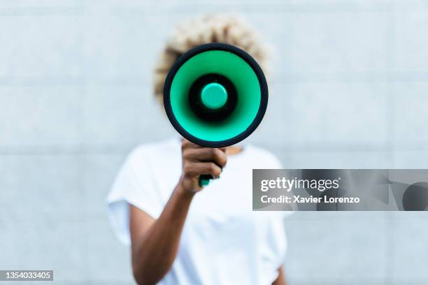 front view of an afro american woman shouting through a megaphone while standing outdoors on the street. - comunicar fotografías e imágenes de stock