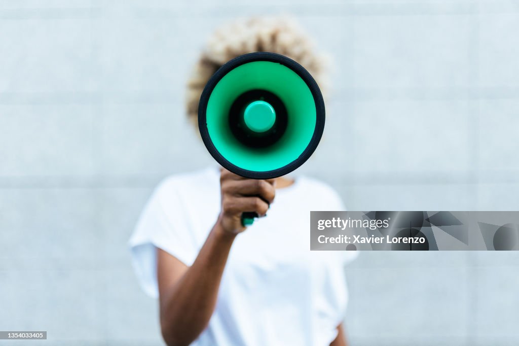 Front view of an afro american woman shouting through a megaphone while standing outdoors on the street.