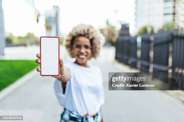 smiling african american woman showing a mobile phone with blank white screen outdoors - tonen stockfoto's en -beelden