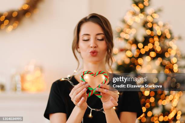 portrait of a positive emotional smiling young woman in a cozy sweater having fun rejoicing preparing for the christmas holiday holding sweet candy and cookies in a decorated room at home during the new year vacation in winter indoor - christmas fun photos et images de collection