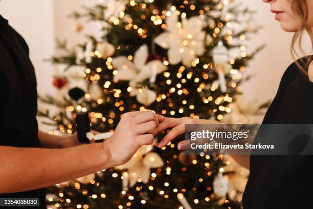 a boyfriend in love makes a marriage proposal to his girlfriend on a christmas holiday in a decorated house in winter. surprised young woman rejoices in a christmas surprise gift an engagement ring - wedding gift stockfoto's en -beelden