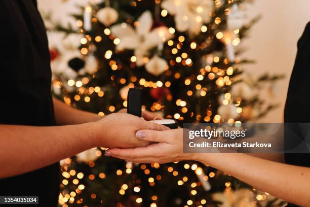 a boyfriend in love makes a marriage proposal to his girlfriend on a christmas holiday in a decorated house in winter. surprised young woman rejoices in a christmas surprise gift an engagement ring - wedding gift stockfoto's en -beelden