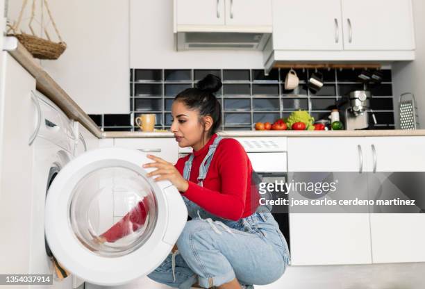 latin woman is at home in the kitchen she opens the door of the washing machine to take out her newly washed clothes - washing machine stock pictures, royalty-free photos & images