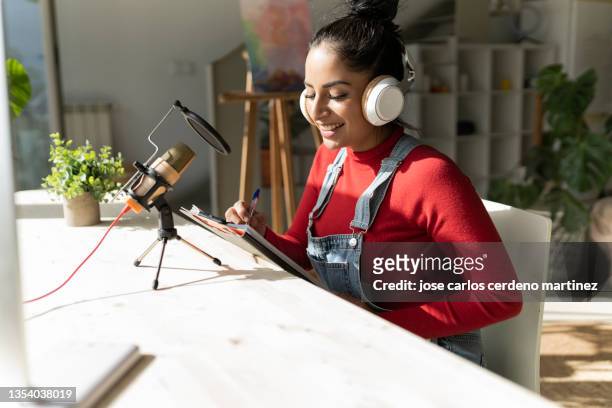 attractive smiling woman in red sweater sits at home recording a podcast - marketing channels stock pictures, royalty-free photos & images