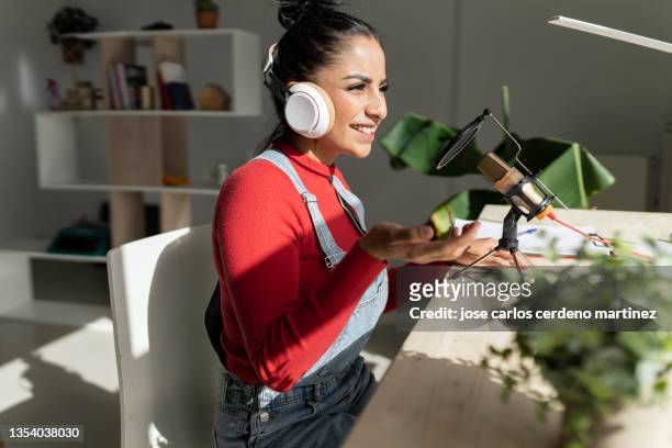latin woman is recording a smiling podcast on her desk in her very bright and cozy home - content stock-fotos und bilder