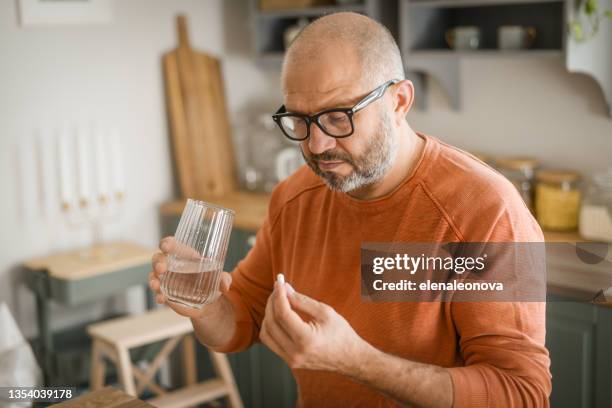 reifer erwachsener mann in gemütlichem interieur der heimischen küche (einnahme von medikamenten) - adults and pills stock-fotos und bilder