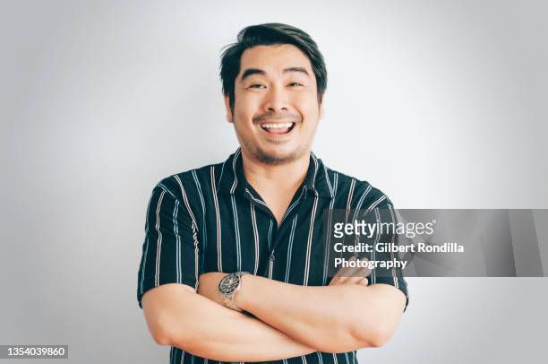 portrait of man with arms crossed standing against white background making funny face - pinoy 個照片及圖片檔