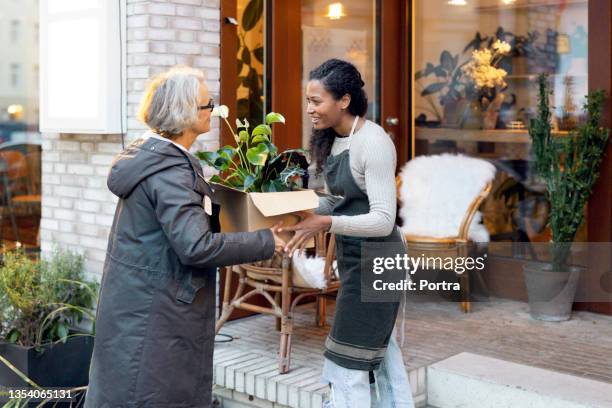 florist handing over plants to customer - flower shop stockfoto's en -beelden