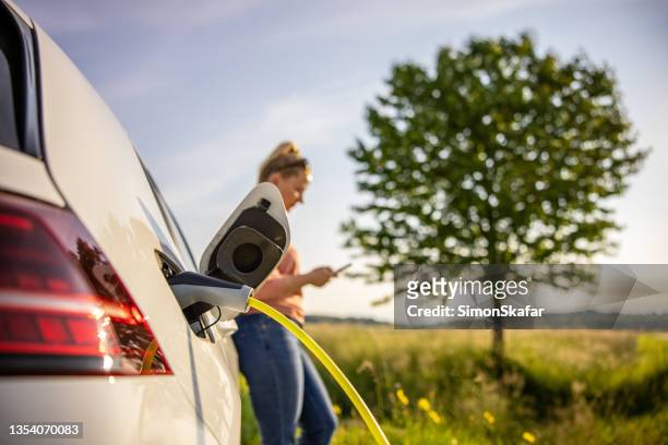 frau mit handy beim aufladen des elektroautos - fuel efficient stock-fotos und bilder