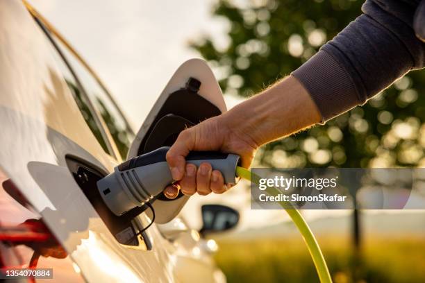 l'uomo inserisce un cavo di alimentazione in un'auto elettrica per la ricarica nella natura - luomo e la macchina foto e immagini stock