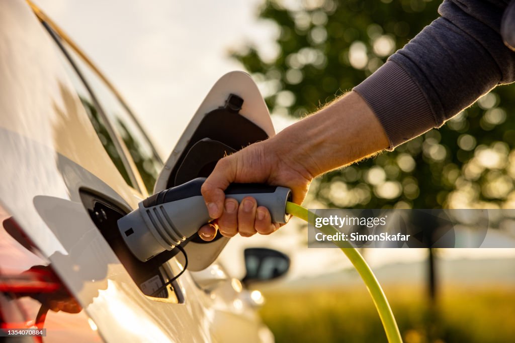Man inserts a power cord into an electric car for charging in the nature