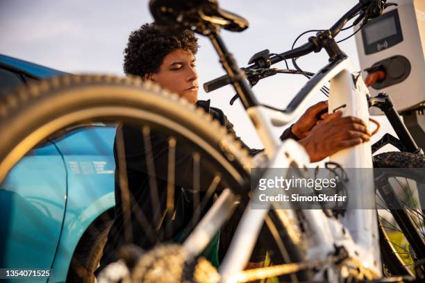 giovane che inserisce la spina nella bicicletta elettrica per la ricarica - electrical plug foto e immagini stock