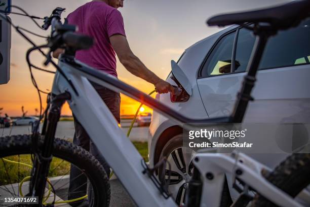 mann steckt elektrischen stecker in auto zum aufladen - e bike stock-fotos und bilder