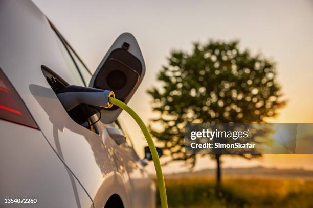 charging an electric car on rural field - elektrische auto stockfoto's en -beelden