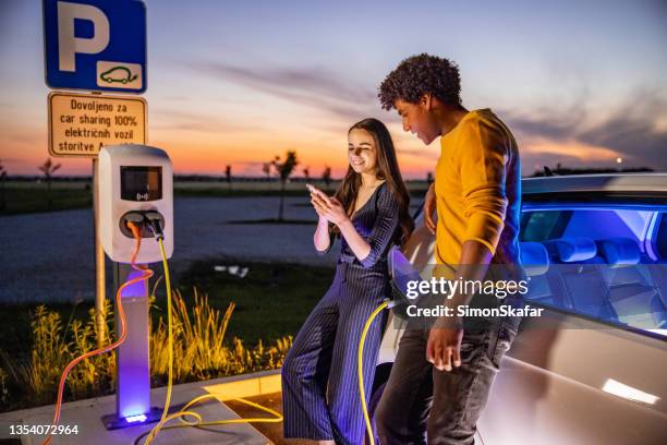 couple using mobile phone while their electric car is charged - station stock pictures, royalty-free photos & images