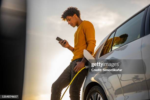 man using mobile phone while charging electric car - elektrische auto stockfoto's en -beelden