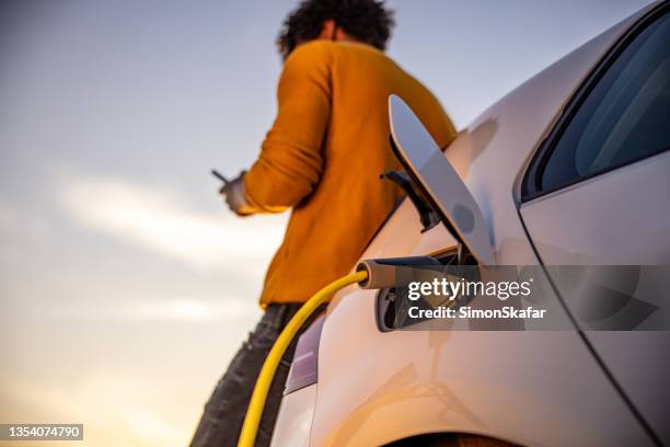 man using mobile phone while charging electric car - elektrische auto stockfoto's en -beelden